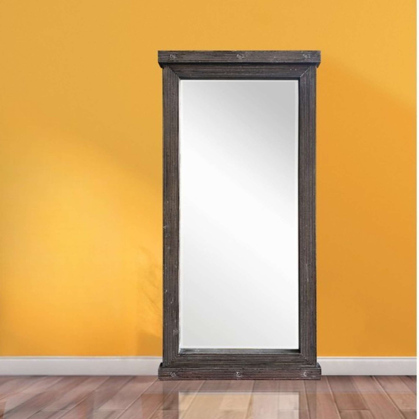 A tall grey wooden beveled wall mirror against a yellow wall with a wooden floor.