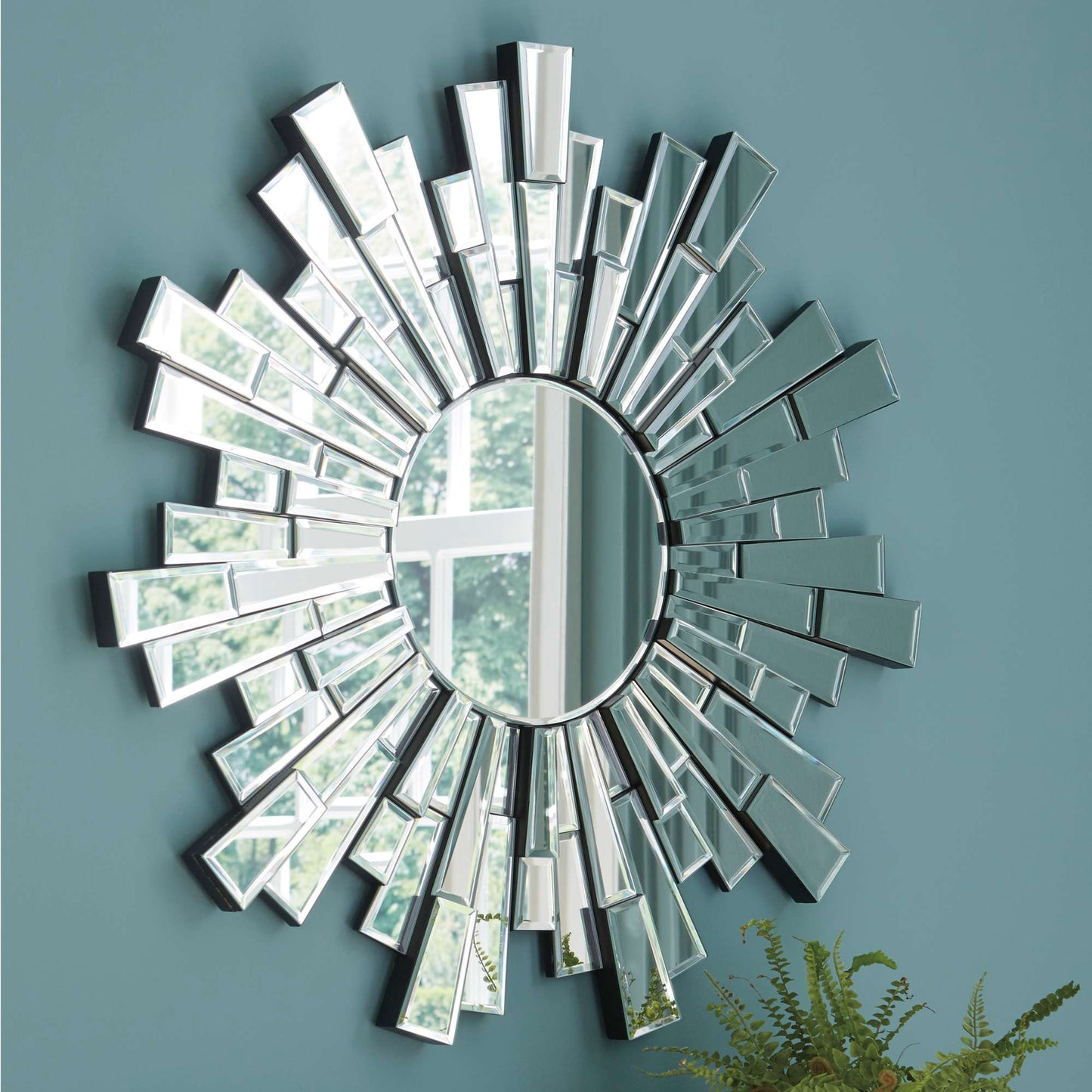 Decorative wall mirror with sunburst design on a teal wall.