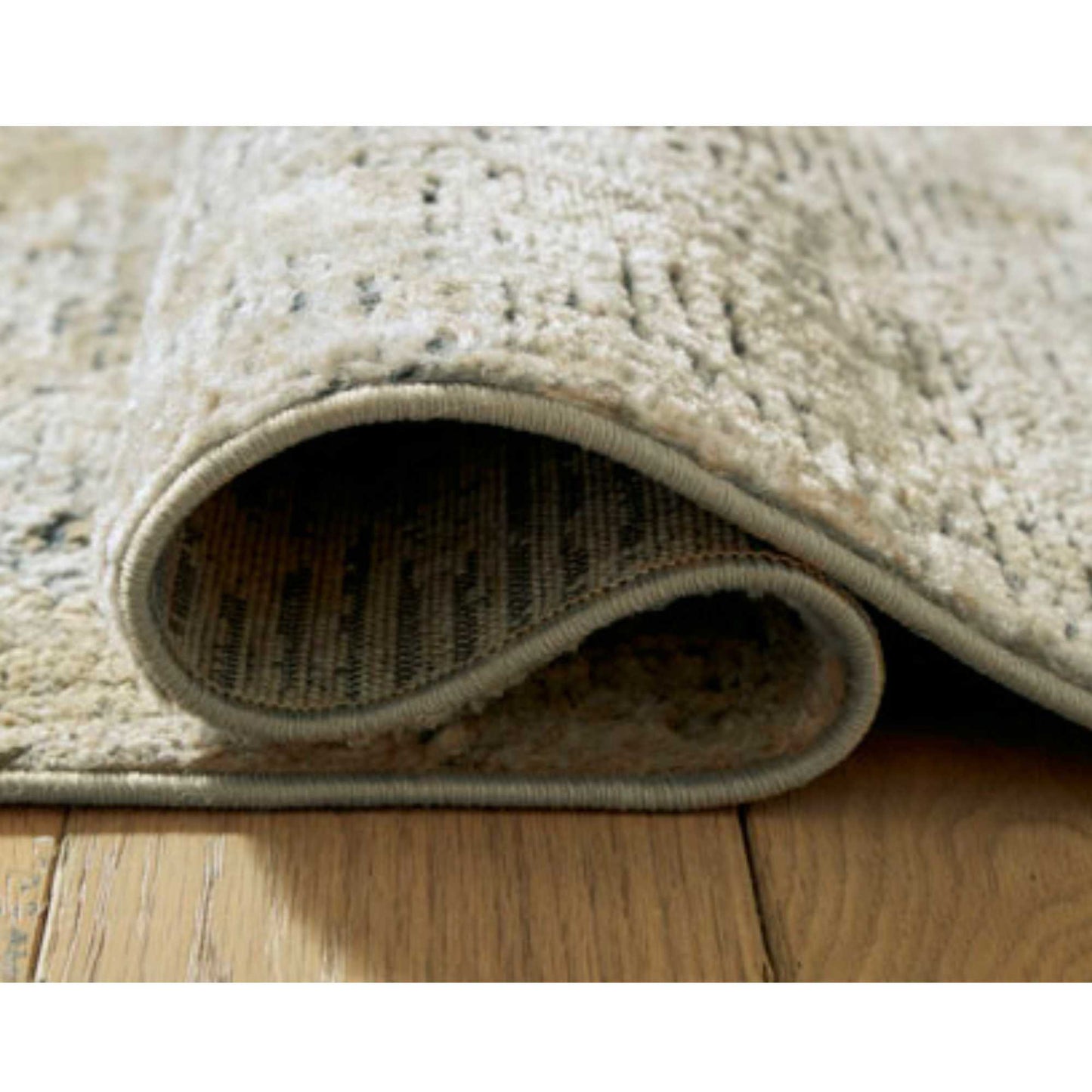 A multi-colored brown area rug with a textured pattern, approximately 5' x 7' in size thats rolled up and on wooden brown floors