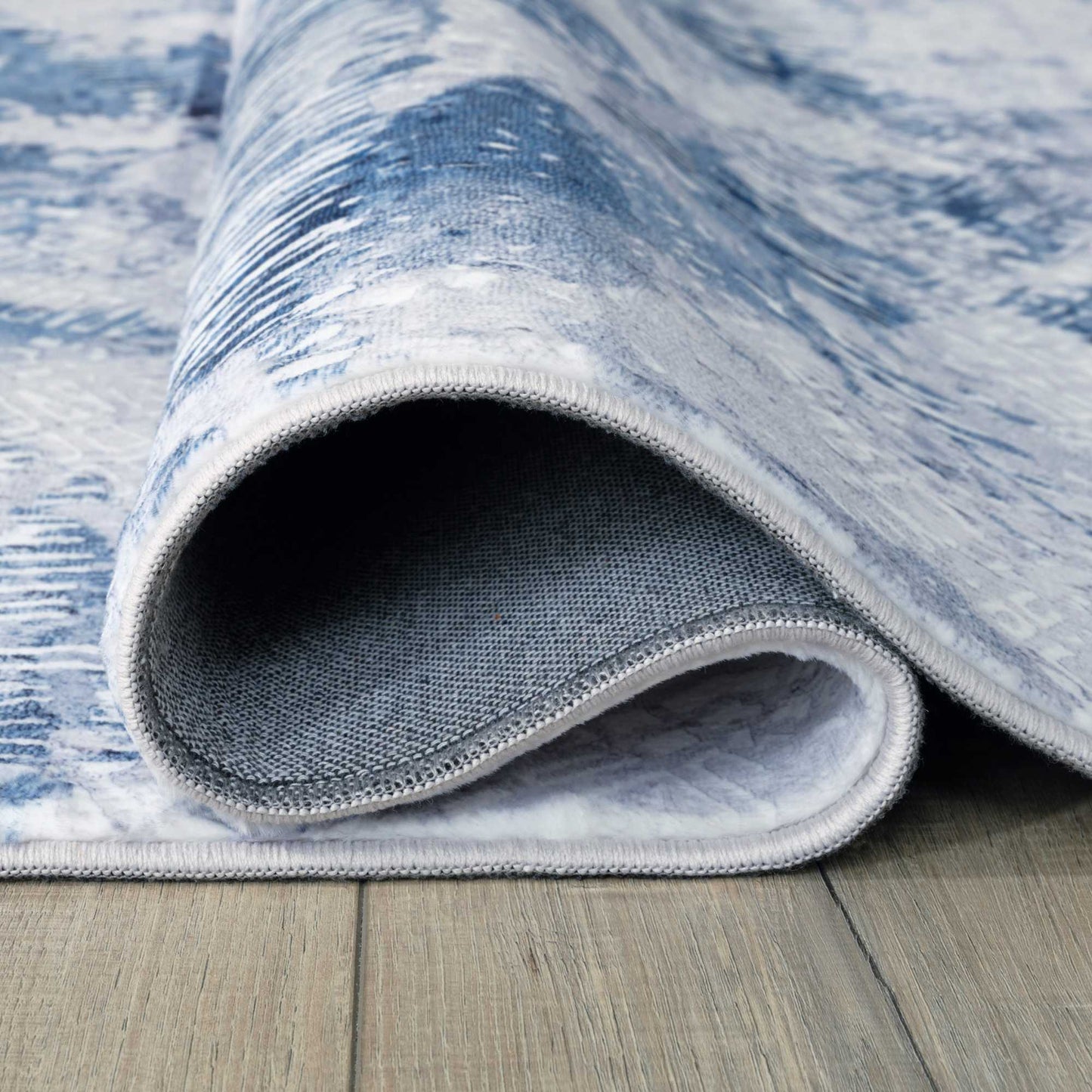 folded rolled blue white stroked area rug on brown wooden floor