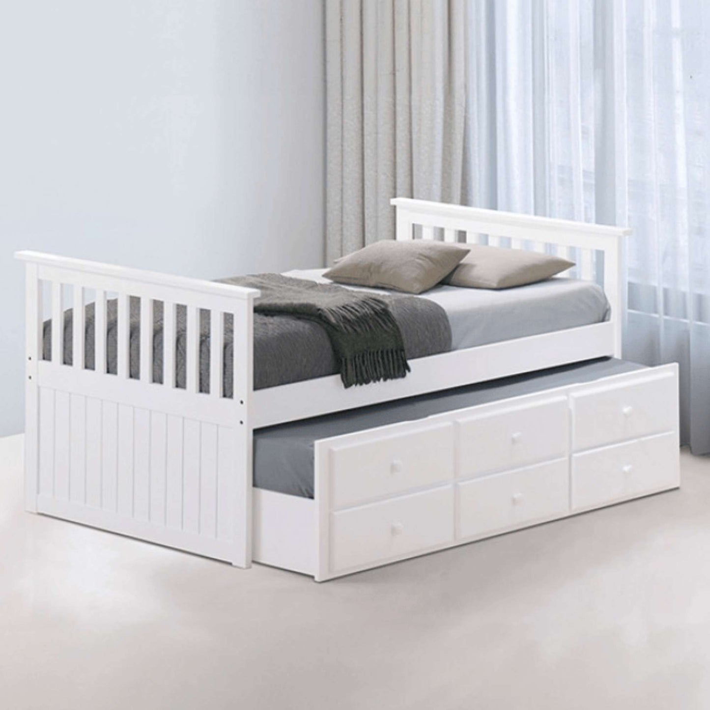 A white twin daybed with a trundle bed and three bottom drawers, displayed in a room setting with bedding and pillows.