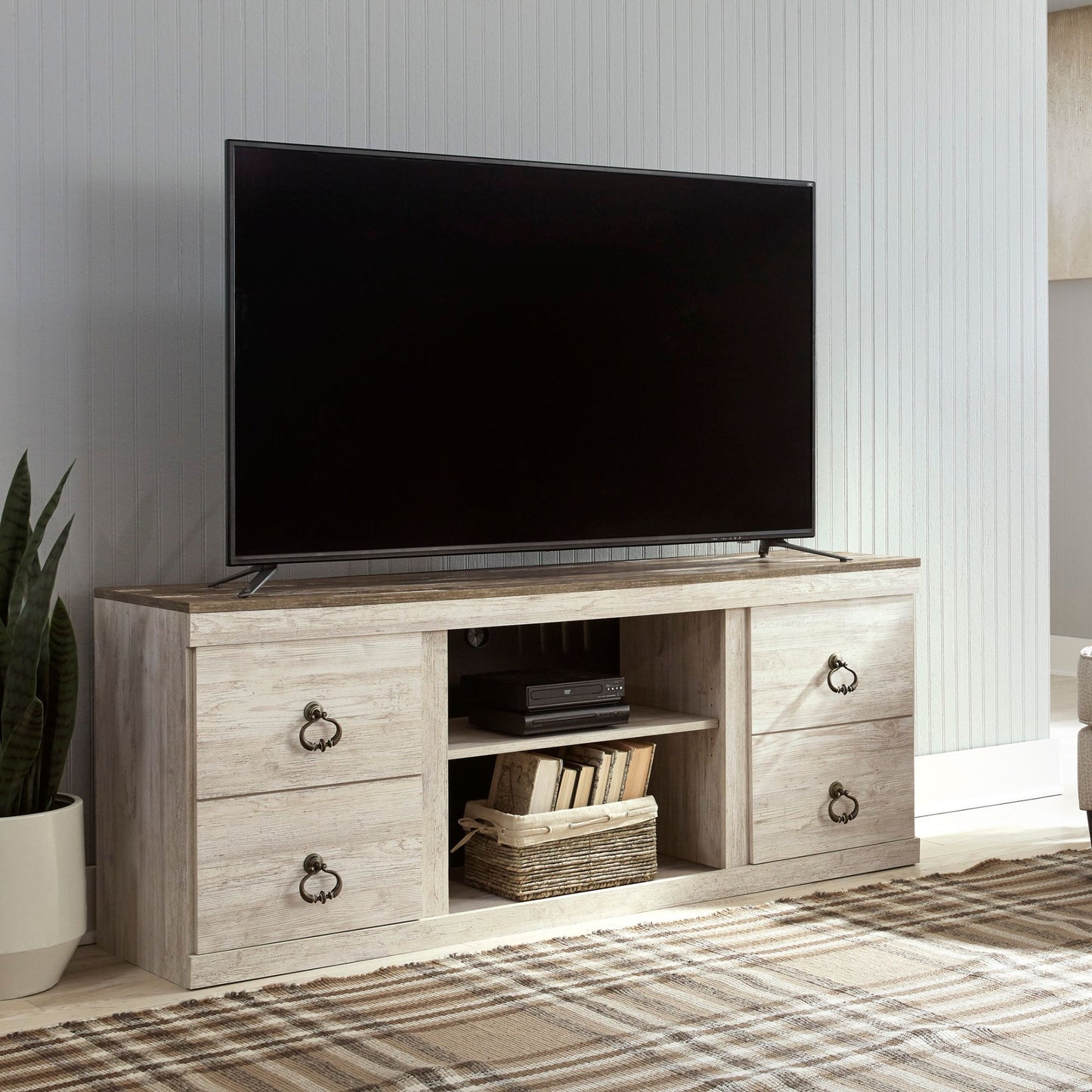 TV on the Arden TV stand in whitewash in a living room setting with a plant and rug.