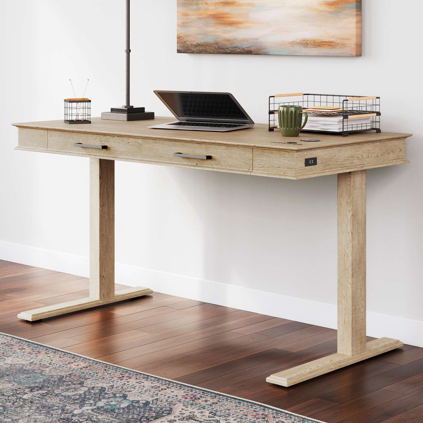 An adjustable height desk in light brown color with a laptop, a monitor, a potted plant, and a wire basket on top.