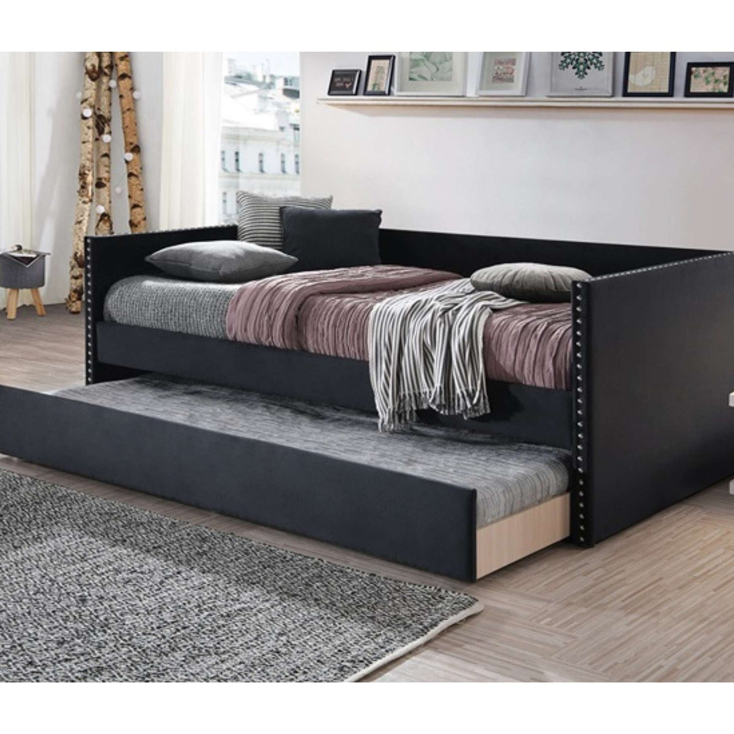 Black twin daybed with trundle in a bedroom setting, featuring gray and pink bedding with nailhead trim on the arms.