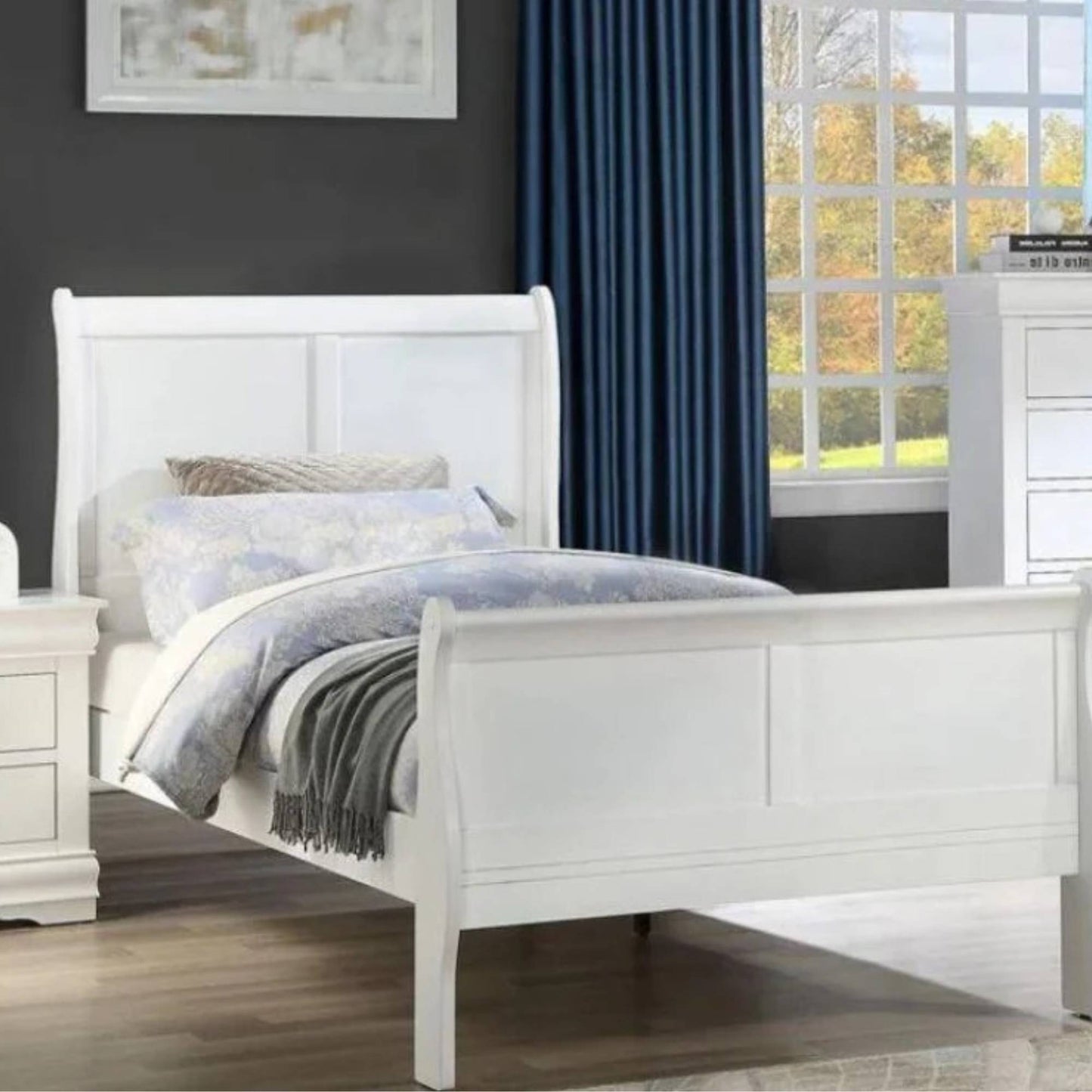 A white twin-sized bedframe with a headboard, footboard, and rails. The bed is dressed with a blue and white bedding set, and the room has a window with blue curtains in the background.