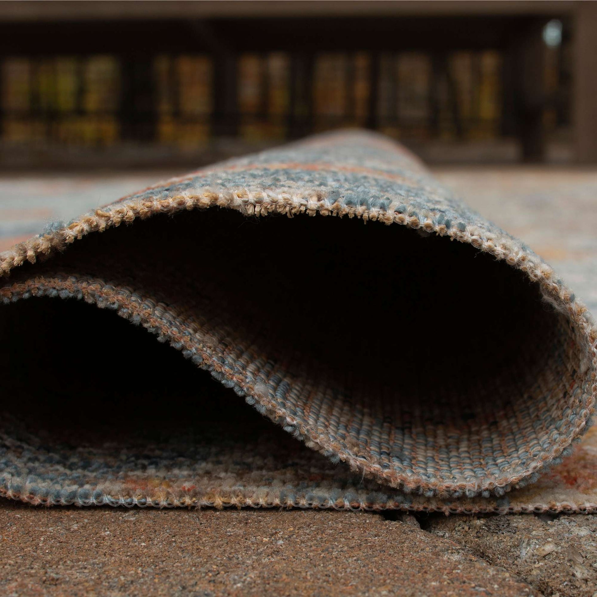 Rolled-up R405051 area rug with multi colored blues, browns and oranges on a concrete floor with blurred background