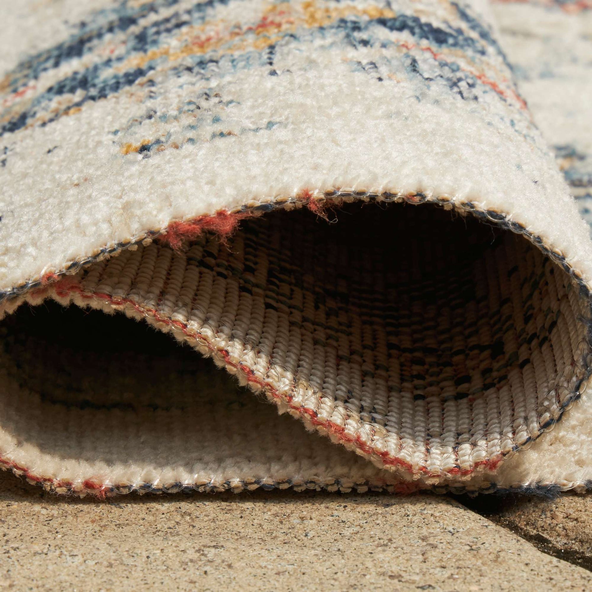 Rolled-up multicolored patterned rug on a textured outdoor surface