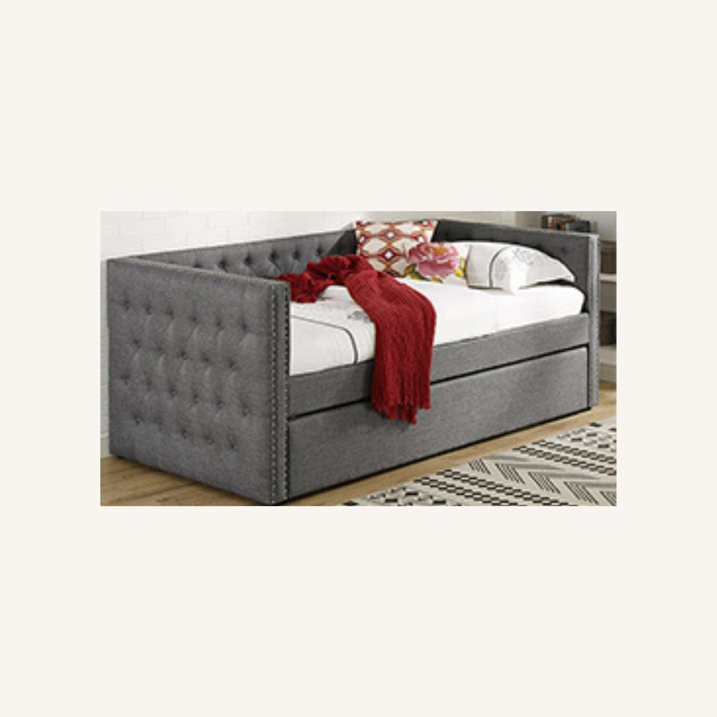Gray upholstered bed with white mattress and red blanket on a wooden floor.