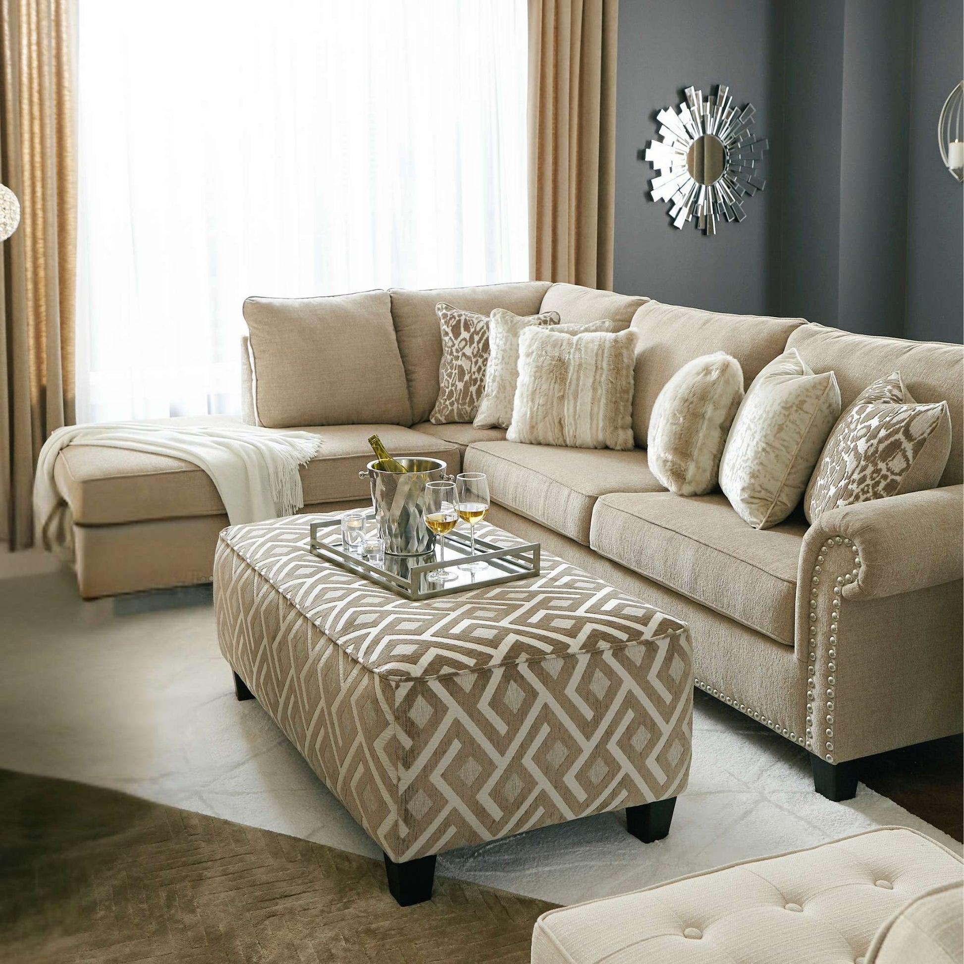 Living room with beige sectional sofa, patterned ottoman, and decorative mirror.