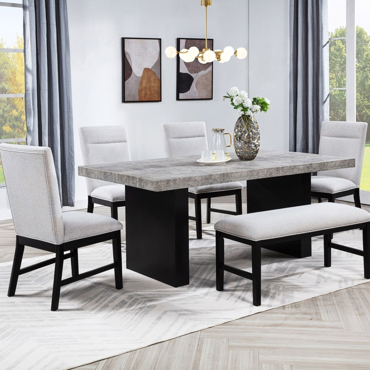 Burleigh 6 PC modern dining room set featuring a rectangular table with a gray concrete-look top and black block pedestal base, surrounded by four upholstered dining chairs with light gray fabric and black legs, plus a matching bench. The set is styled in a bright room with gray curtains, a white rug, and a chandelier.