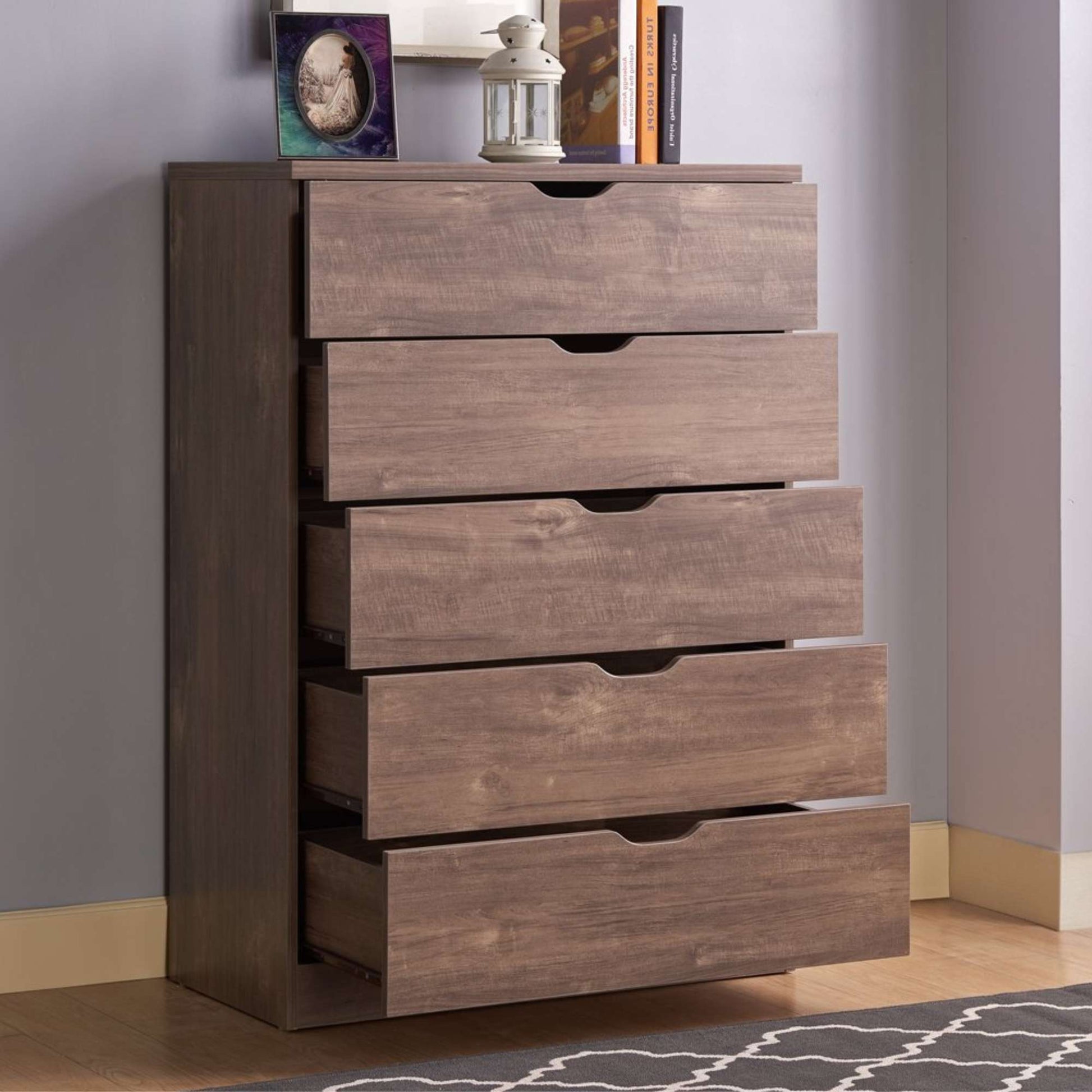 Wooden dresser with five drawers against a gray wall.