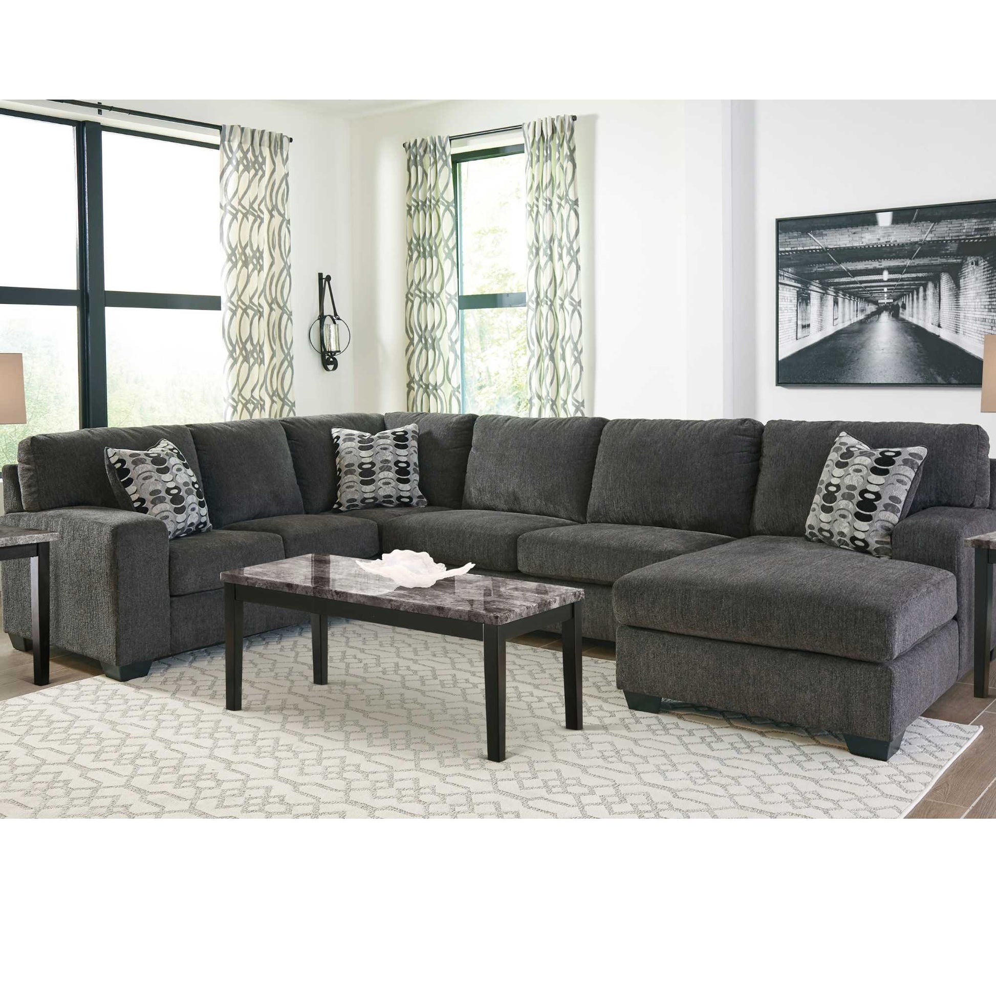 A 3-piece sectional sofa with chaise, smoke gray upholstery, displayed in a living room setting with accent pillows, throw rugs, and a coffee table.