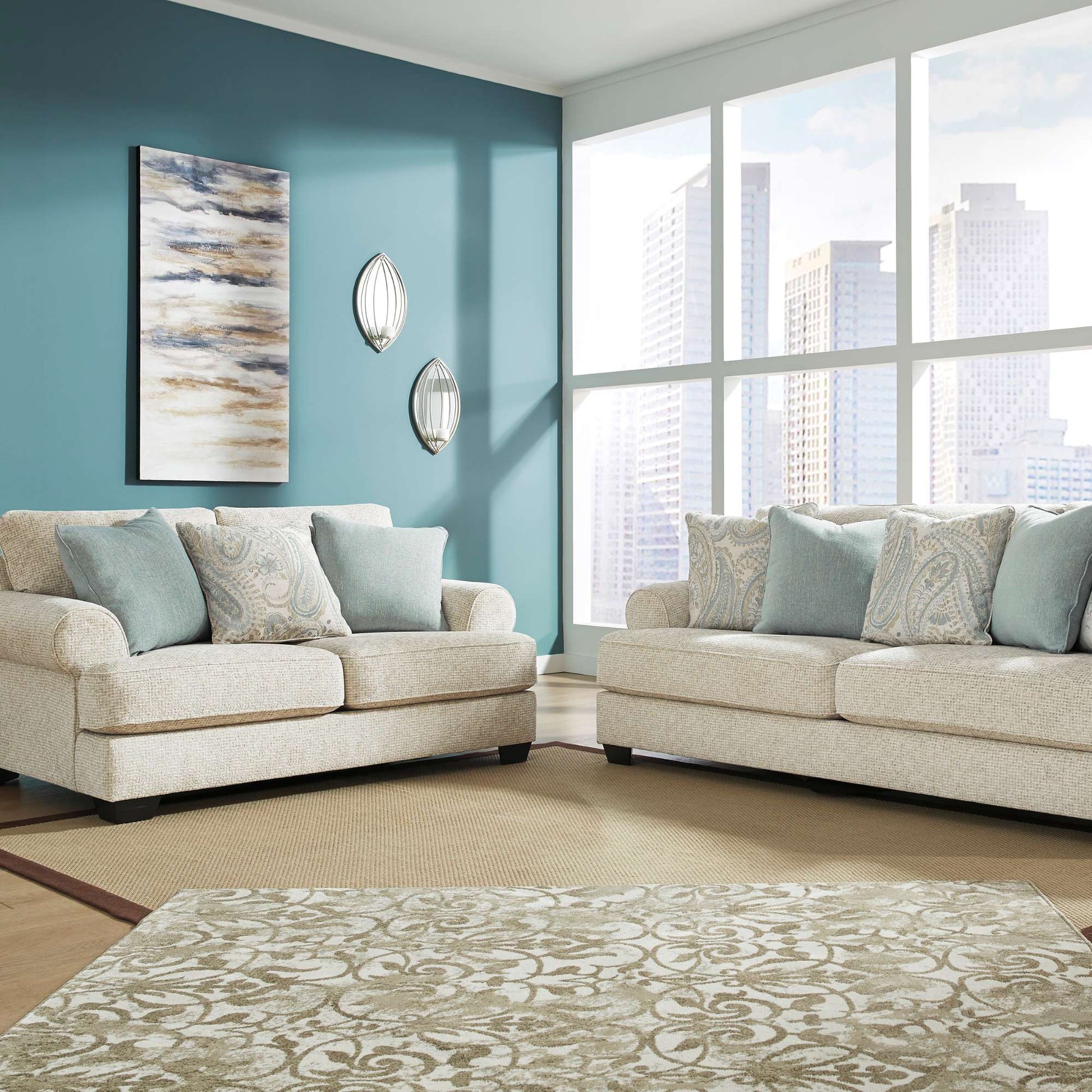 Living room with beige sofa and loveseat, light blue walls, and large windows.