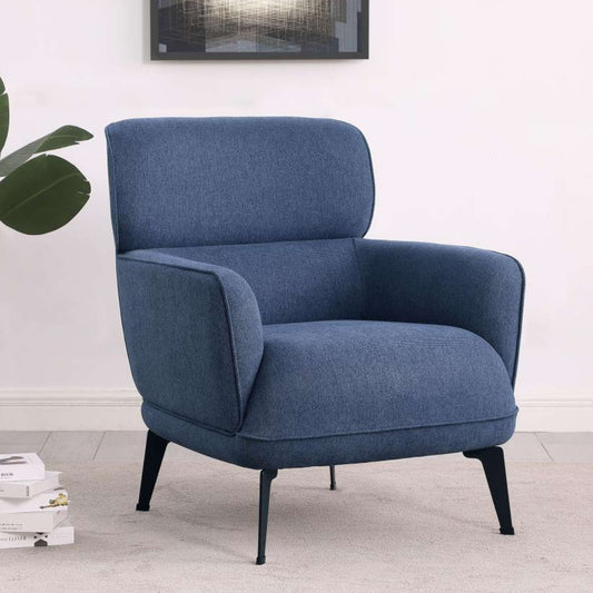 A blue upholstered accent chair with crescent arms and black metal legs, positioned in a room with a plant and decorative books.