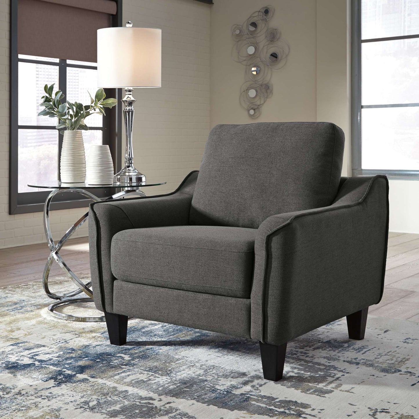 Gray armchair in a living room setting with a lamp and decorative elements.