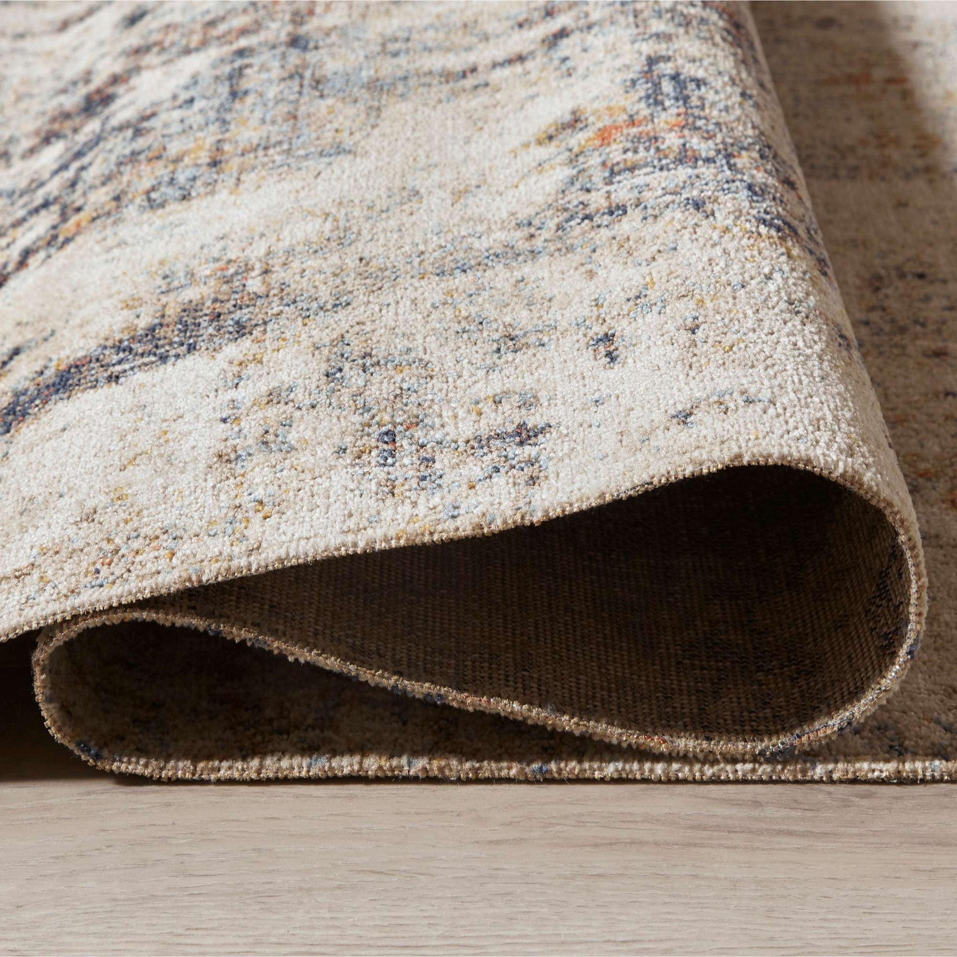 Close-up of a textured area rug with a neutral color palette on a wooden floor.